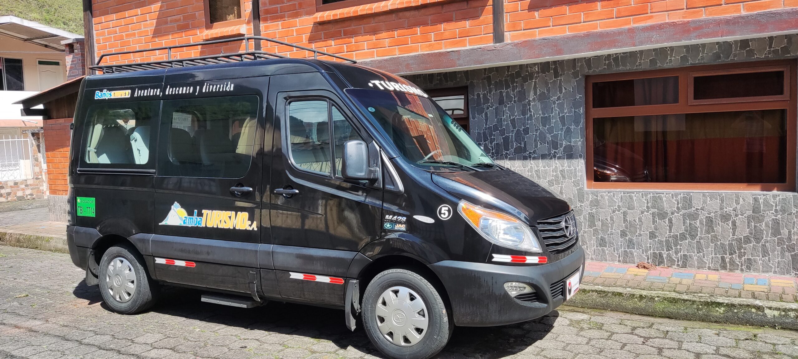 Van de Ambaturismo C.A. estacionada en zona urbana brindando servicio de transporte turístico.