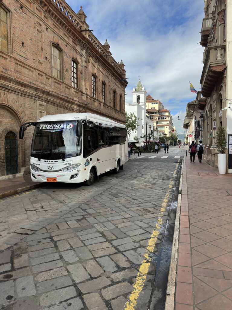 Bus de Ambaturismo C.A. realizando transporte turístico en el centro histórico de Cuenca, Ecuador.